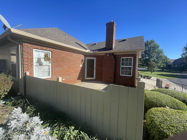 back of property with a shingled roof, fence private yard, brick siding, and a chimney