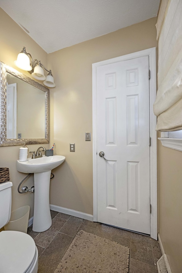 half bath with toilet, stone finish flooring, and baseboards