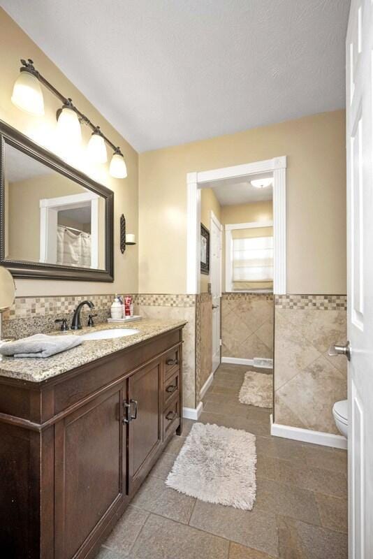 full bath featuring vanity, toilet, tile walls, and wainscoting