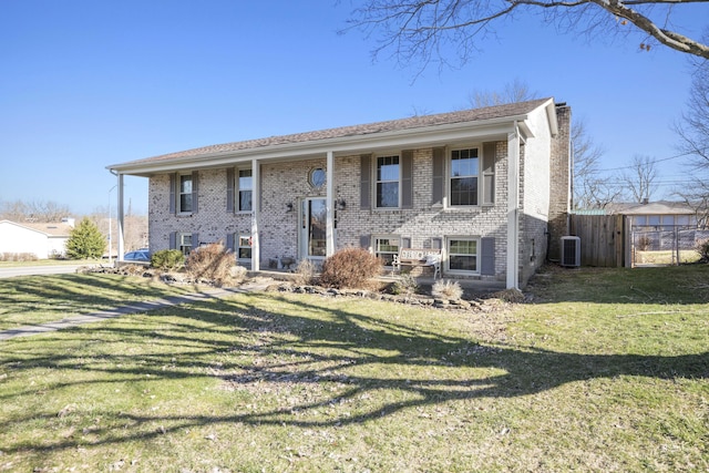 bi-level home featuring a front lawn, brick siding, central AC, and a chimney