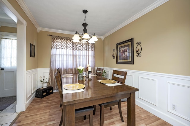 dining area featuring light wood-style flooring, ornamental molding, wainscoting, and a chandelier