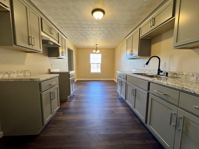 kitchen with gray cabinets, a sink, under cabinet range hood, dark wood finished floors, and baseboards