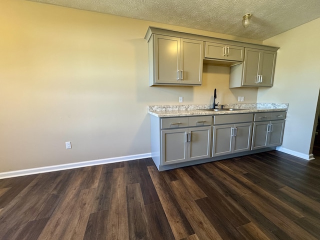 kitchen featuring a sink, baseboards, gray cabinetry, and dark wood-style flooring