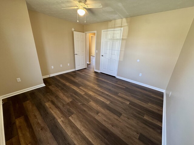 unfurnished bedroom featuring dark wood-style floors, a textured ceiling, baseboards, and a ceiling fan