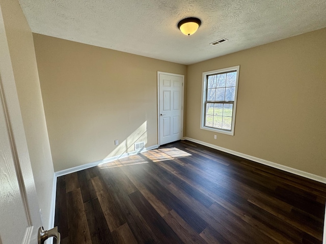 empty room featuring baseboards, visible vents, dark wood-style flooring, and a textured ceiling