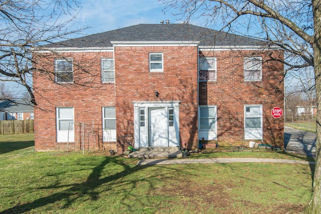 rear view of property featuring brick siding, roof with shingles, a lawn, and fence