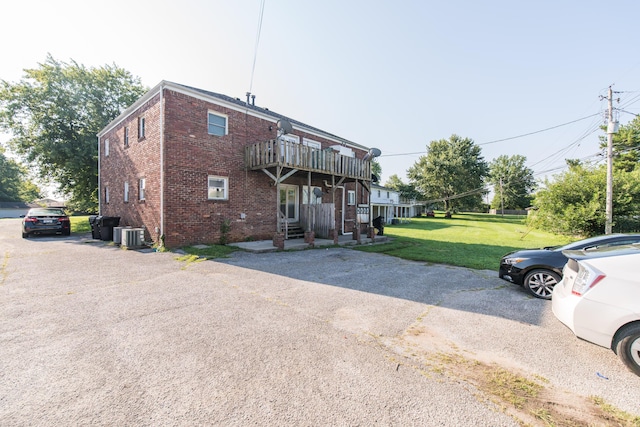 rear view of house featuring central air condition unit, a lawn, and brick siding