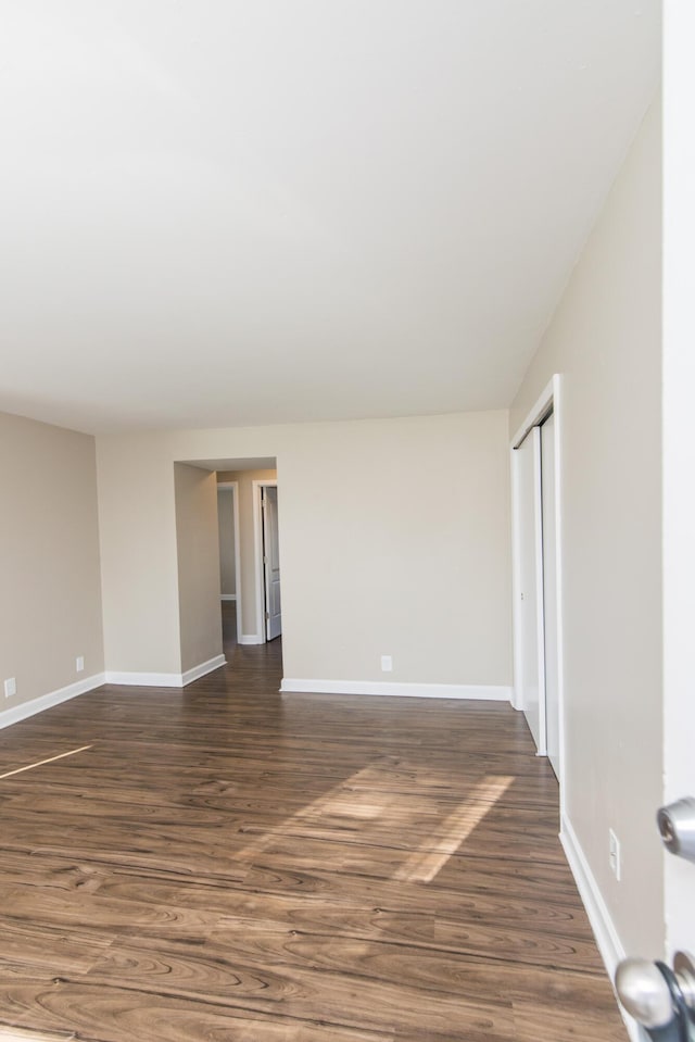 spare room with dark wood-type flooring and baseboards