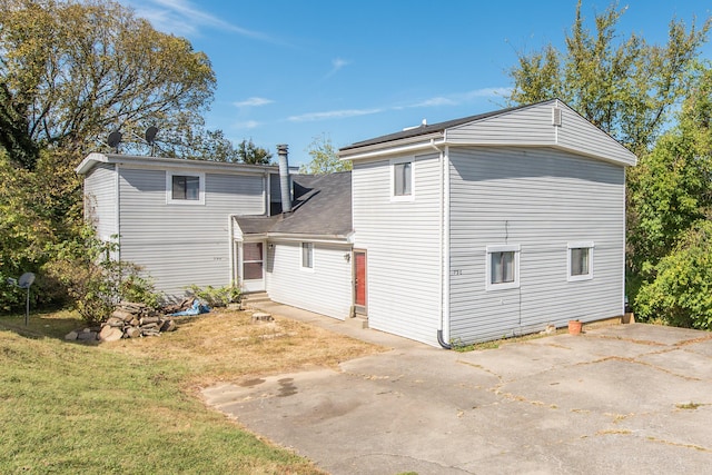 rear view of house featuring entry steps, concrete driveway, and a lawn