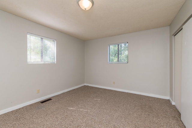 unfurnished bedroom featuring visible vents, carpet flooring, a textured ceiling, and baseboards