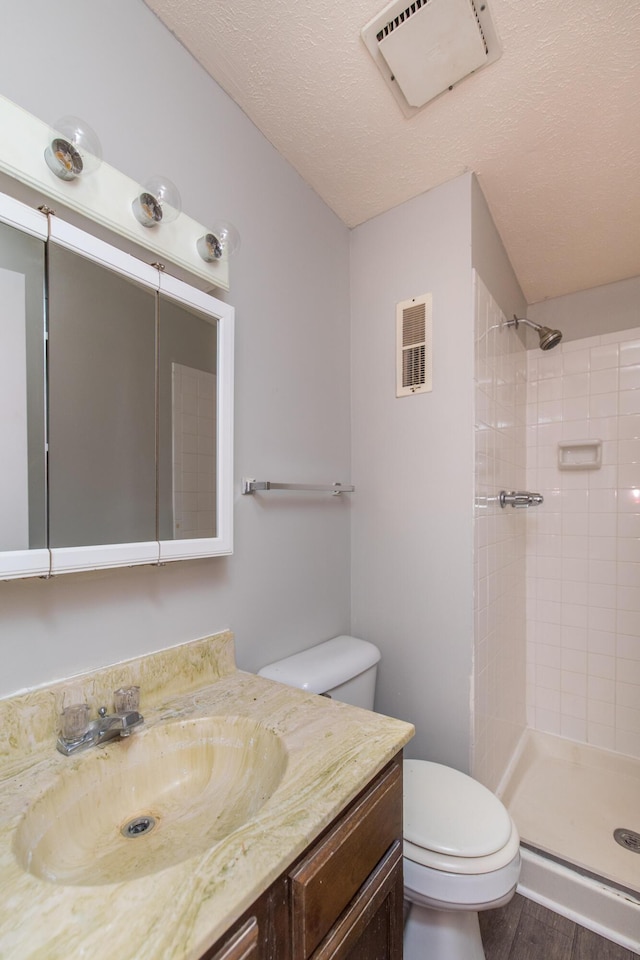 bathroom with visible vents, toilet, vanity, and a tile shower