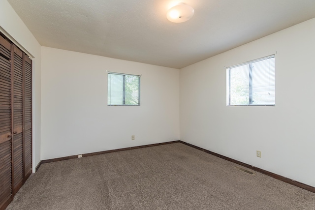 unfurnished bedroom with multiple windows, carpet, visible vents, and a closet