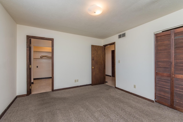 unfurnished bedroom featuring a closet, carpet floors, a textured ceiling, and visible vents