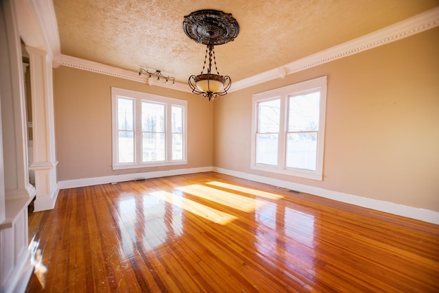 empty room with an inviting chandelier, wood-type flooring, visible vents, and ornate columns