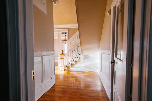 hallway with stairs, wood-type flooring, wainscoting, crown molding, and a decorative wall