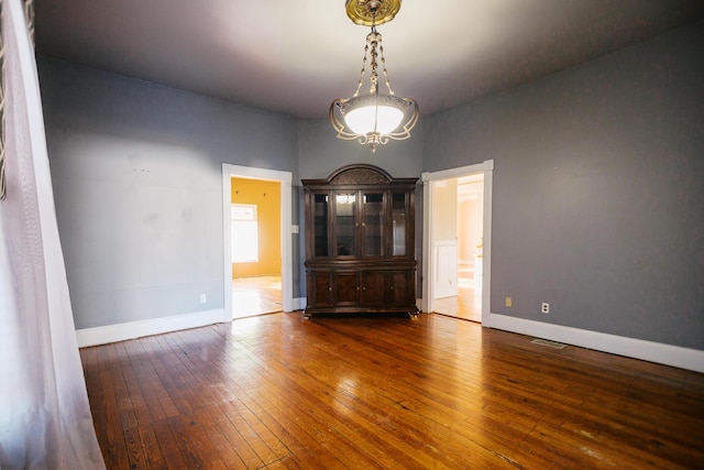 empty room with a notable chandelier, visible vents, baseboards, and wood-type flooring