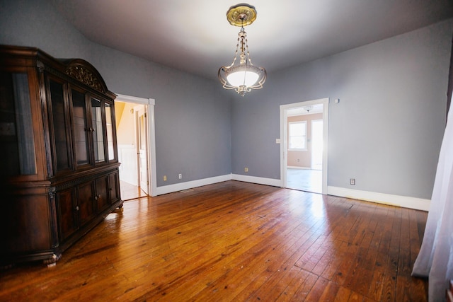 unfurnished room featuring an inviting chandelier, baseboards, and dark wood-style flooring