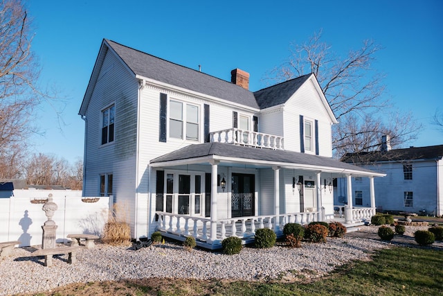 view of front facade featuring a porch, fence, roof with shingles, a balcony, and a chimney