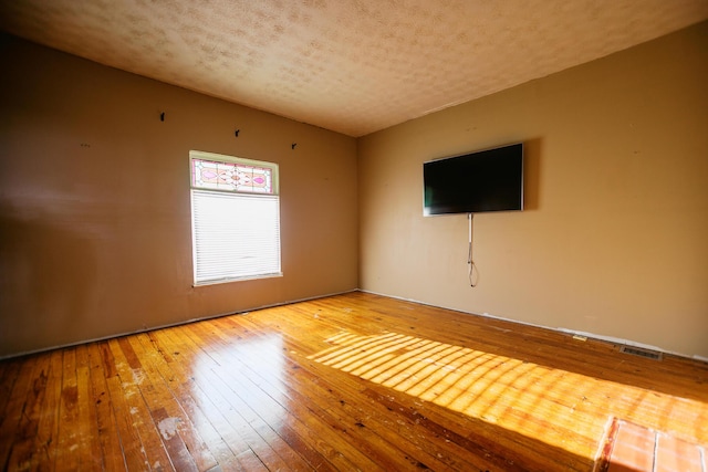 unfurnished room featuring hardwood / wood-style floors, visible vents, and a textured ceiling