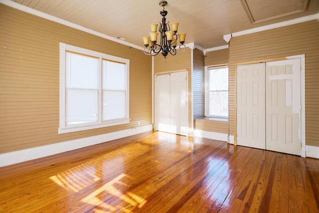 unfurnished bedroom with multiple closets, a notable chandelier, ornamental molding, hardwood / wood-style floors, and baseboards