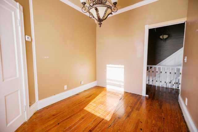 unfurnished room featuring baseboards, a notable chandelier, crown molding, and hardwood / wood-style flooring