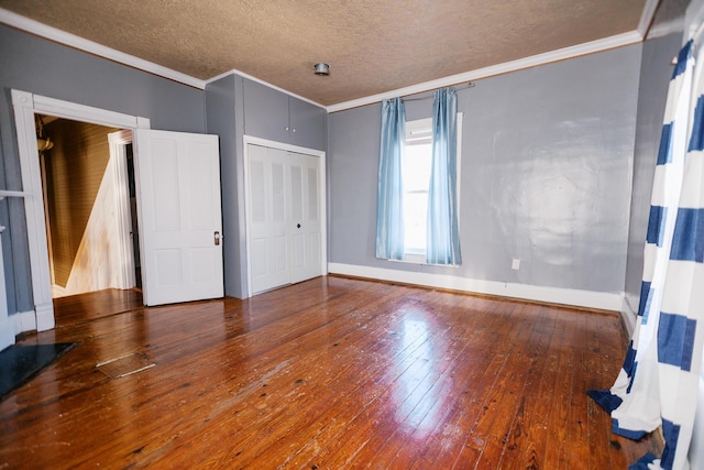 unfurnished bedroom featuring baseboards, hardwood / wood-style flooring, a closet, a textured ceiling, and crown molding