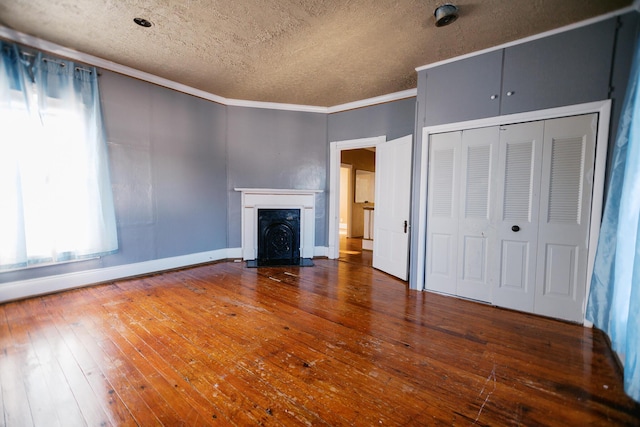 unfurnished living room featuring baseboards, a fireplace with flush hearth, ornamental molding, wood-type flooring, and a textured ceiling