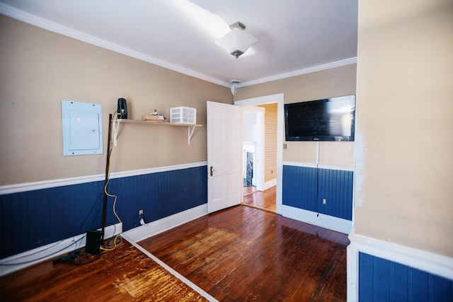 interior space featuring electric panel, a wainscoted wall, crown molding, and wood-type flooring