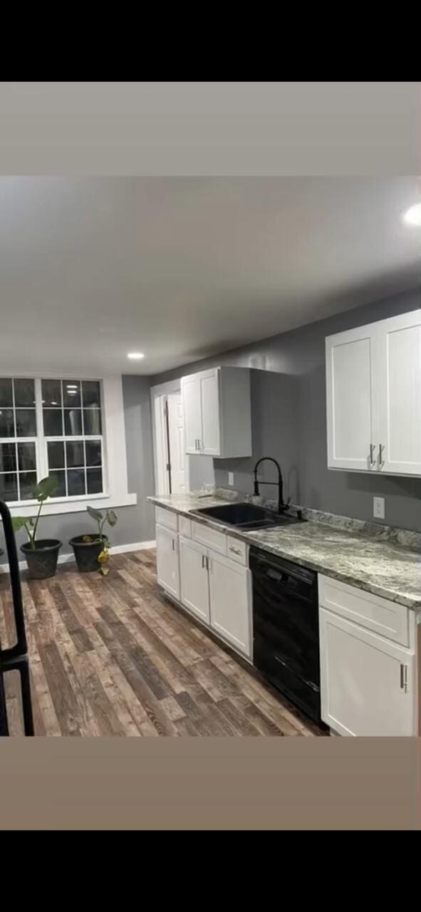 kitchen featuring baseboards, dishwasher, wood finished floors, white cabinetry, and a sink