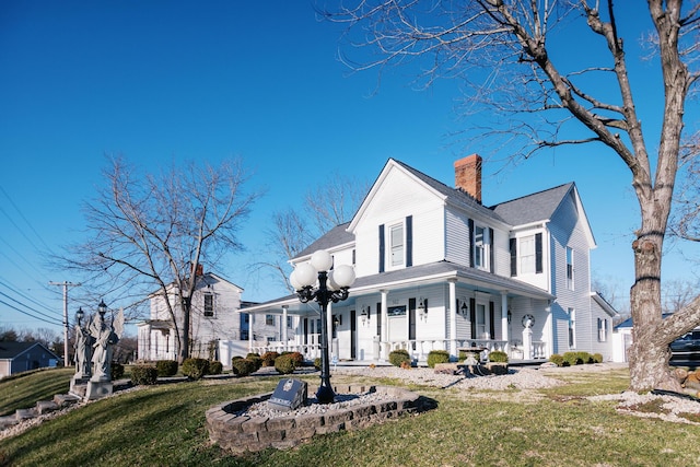 view of front of house with covered porch, a chimney, and a front lawn