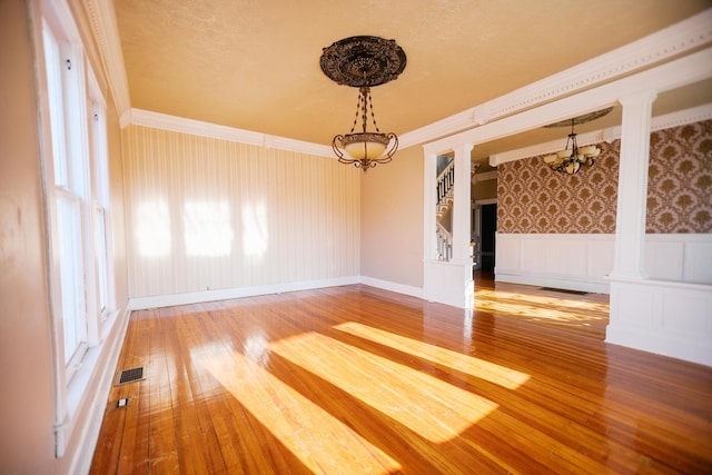 spare room with hardwood / wood-style flooring, an inviting chandelier, wainscoting, wallpapered walls, and ornate columns