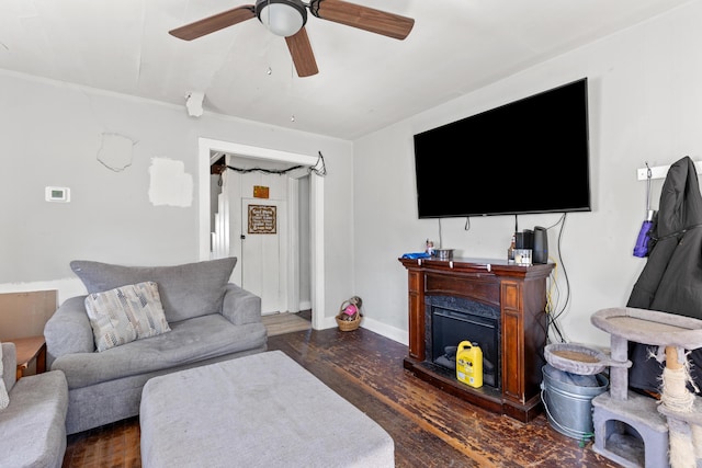 living area with a fireplace with raised hearth, baseboards, a ceiling fan, and wood finished floors