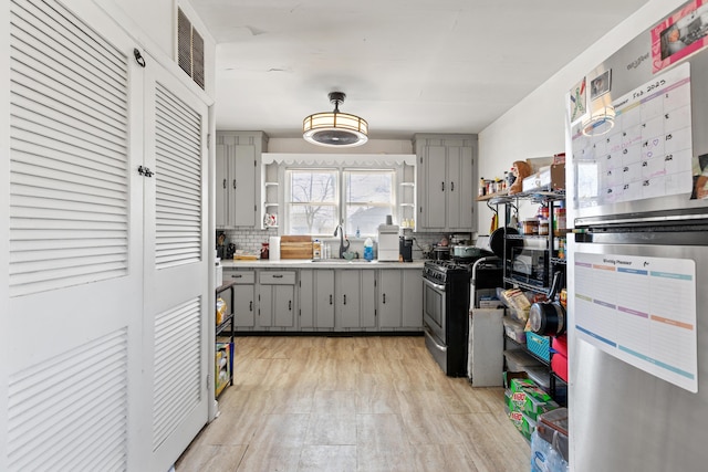 kitchen featuring open shelves, stainless steel range with gas stovetop, gray cabinets, and a sink