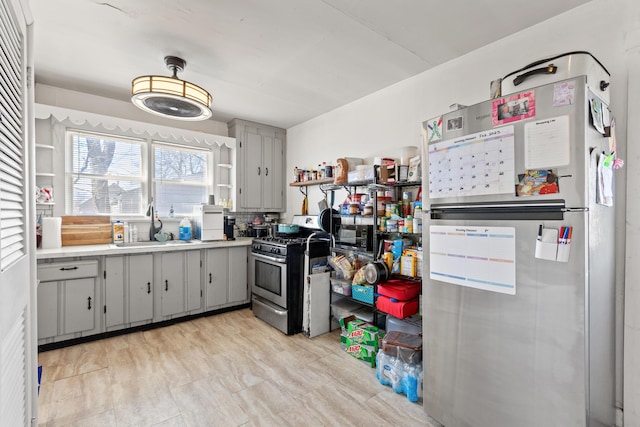 kitchen with open shelves, light countertops, gray cabinets, appliances with stainless steel finishes, and a sink