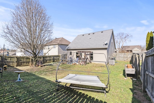 back of property with central AC unit, a lawn, roof with shingles, and a fenced backyard