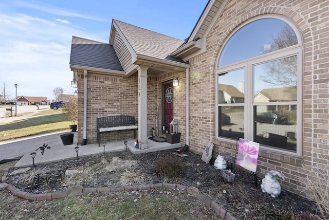 view of exterior entry with brick siding and roof with shingles