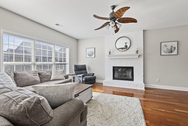 living room featuring wood finished floors, a fireplace, visible vents, and baseboards