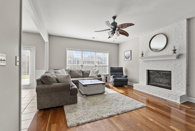 living area with a fireplace, wood finished floors, baseboards, and a ceiling fan