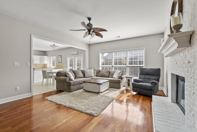 living room featuring visible vents, light wood-style flooring, a ceiling fan, baseboards, and a brick fireplace