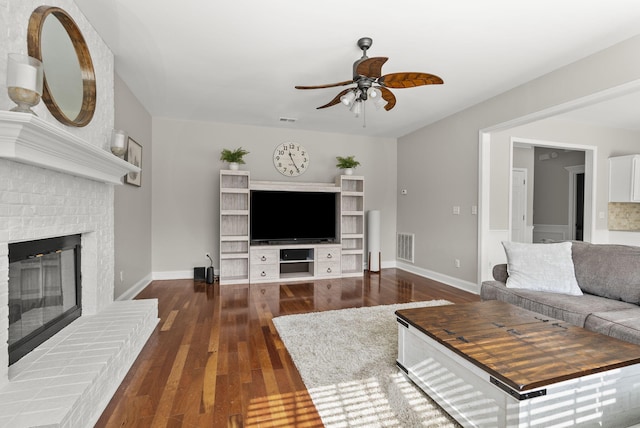 living room featuring a ceiling fan, wood finished floors, visible vents, baseboards, and a brick fireplace