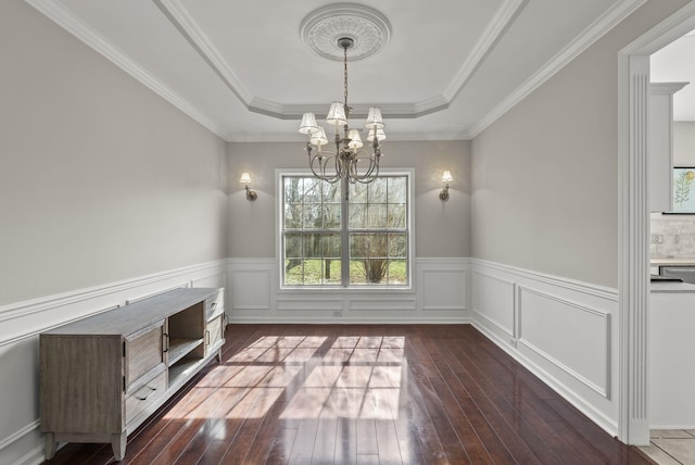 unfurnished dining area featuring hardwood / wood-style floors, wainscoting, crown molding, a raised ceiling, and a chandelier