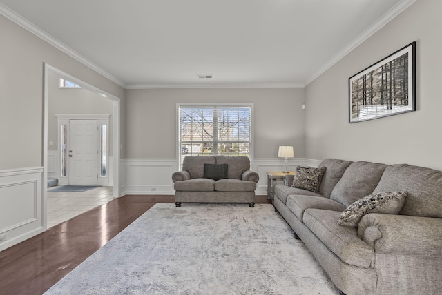 living room with visible vents, ornamental molding, a wainscoted wall, and wood finished floors