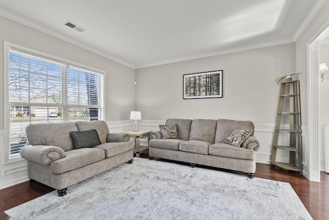 living room featuring a wainscoted wall, visible vents, dark wood-style flooring, and ornamental molding