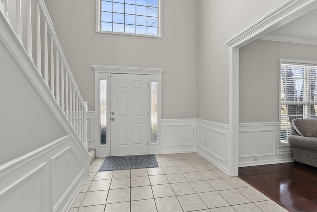 foyer featuring stairs, crown molding, a decorative wall, and light tile patterned floors