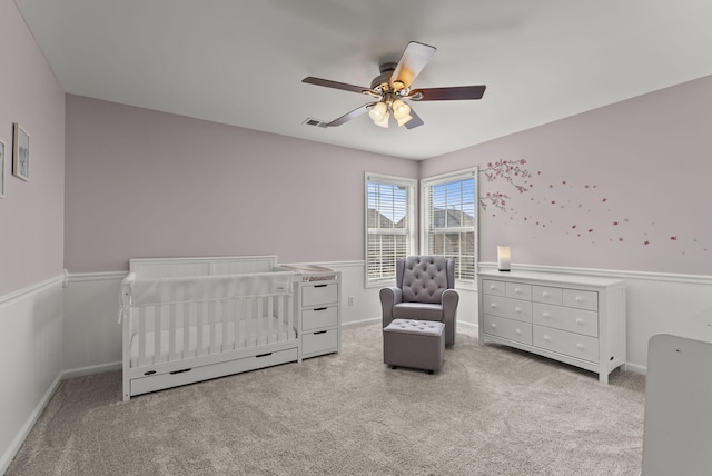 carpeted bedroom with visible vents, a crib, baseboards, and ceiling fan