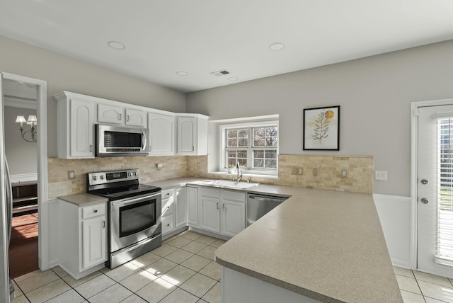 kitchen with visible vents, stainless steel appliances, a peninsula, light tile patterned flooring, and white cabinets