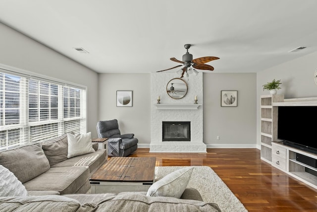 living area featuring visible vents, a brick fireplace, baseboards, and wood finished floors