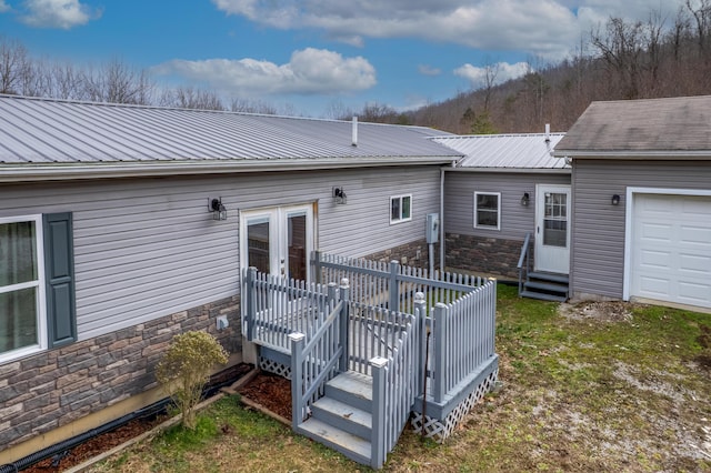 back of property featuring stone siding, entry steps, metal roof, and an attached garage