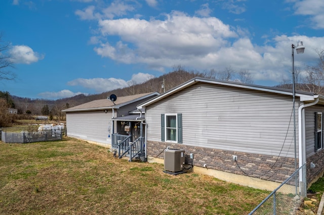 back of house featuring central air condition unit, stone siding, a yard, and fence