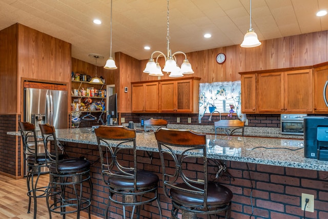 kitchen featuring brown cabinetry, stone counters, light wood-style floors, and stainless steel fridge with ice dispenser